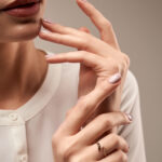 Close up portrait of incognito female model presenting silver ring with black and white stones. Crop of woman posing in studio, isolated on grey background. Concept of expensive jewelry.